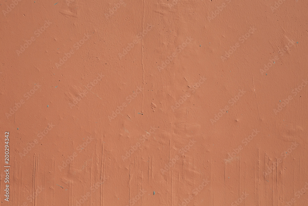 Front close-up view of a cement wall painted in light brown color. There are some particles stuck under the paint layer and brush trails can be clearly seen as well.