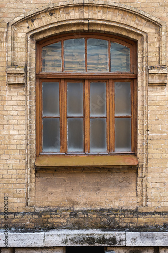 Vintage arched window in the wall of yellow brick. Black glass in a maroon dark red wooden frame. The concept of antique vintage architecture in building elements.