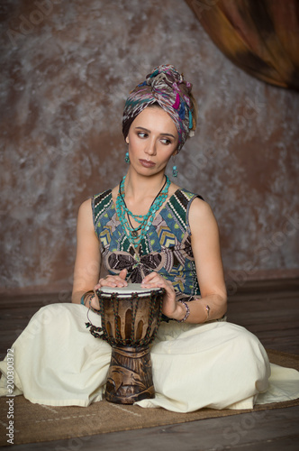 A beautiful girl in a turtleneck plays an ethnic drum in a room with an Oriental interior. photo