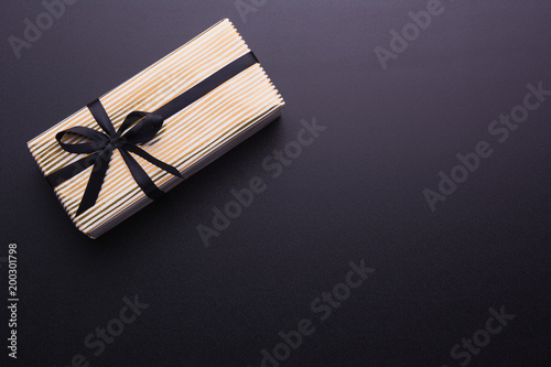 Hands holding wrapped gift box with colored ribbon as a present for Christmas, new year, mother's day, anniversary, birthday, party, on black background, top view. Present for a colleague at work.
