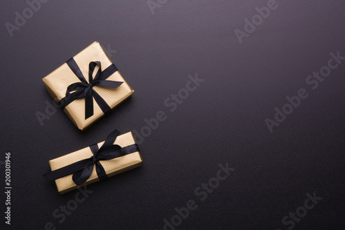 Wrapped gift box with colored ribbon as a present for Christmas, new year, mother's day, anniversary, birthday, party, on black background, top view. Present for a colleague at work.