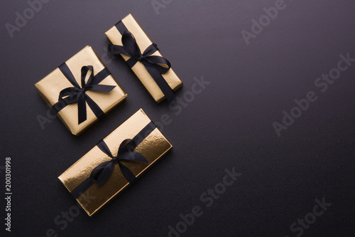 Wrapped gift box with colored ribbon as a present for Christmas, new year, mother's day, anniversary, birthday, party, on black background, top view. Present for a colleague at work.