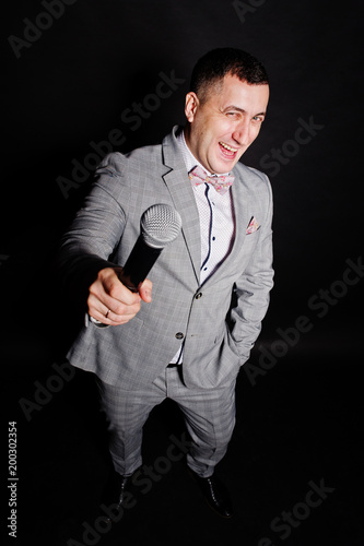 Handsome man in gray suit with microphone against black background on studio. Laughs face of toastmaster and showman.