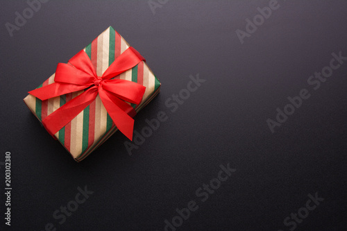 Hands holding wrapped gift box with colored ribbon as a present for Christmas, new year, mother's day, anniversary, birthday, party, on black background, top view. Present for a colleague at work.