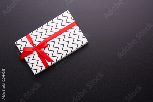 Hands holding wrapped gift box with colored ribbon as a present for Christmas, new year, mother's day, anniversary, birthday, party, on black background, top view. Present for a colleague at work.