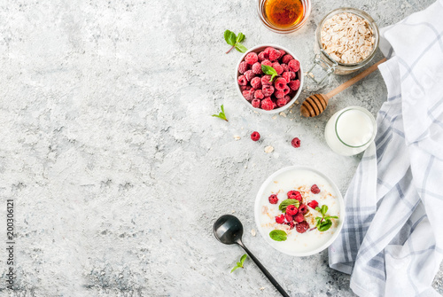 Raw ingredients for summer healthy breakfast  cereals  oats   fresh Raspberry  mint leaves  yoghurt  honey  on light concrete background  top view  copy space
