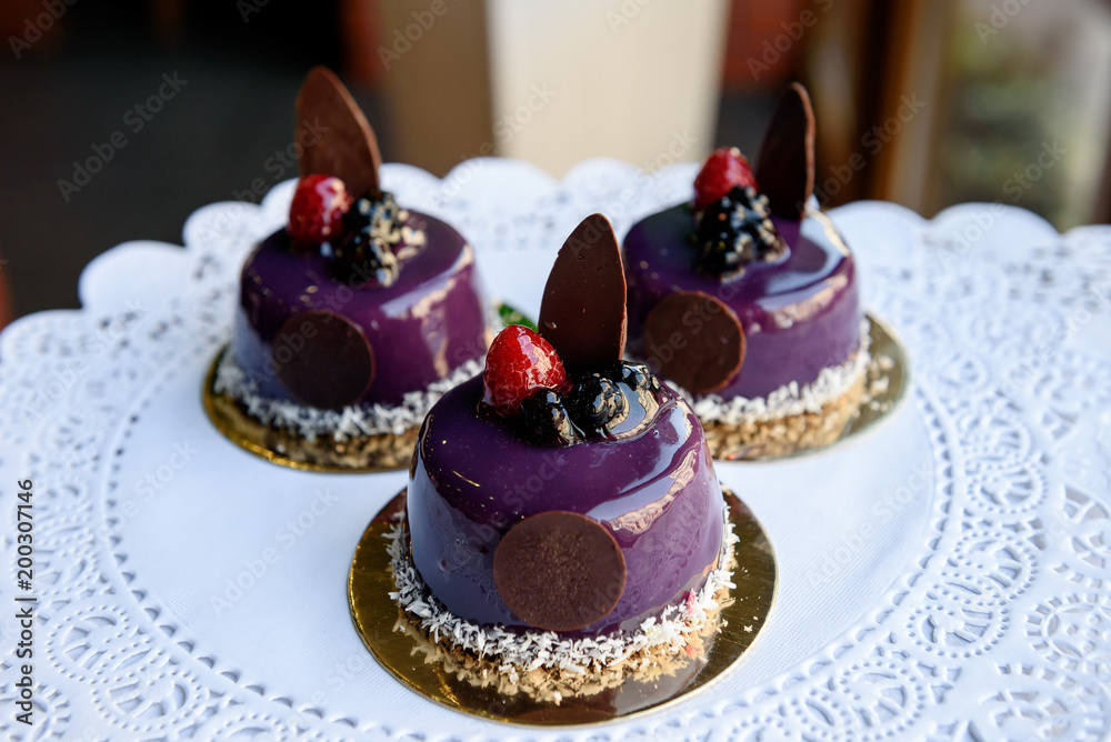 Tasty violet cakes with berries stand on white tablecloth Tasty violet cakes with berries stand on white tablecloth