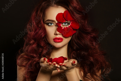 Portrait of beautiful luxury sexy woman with creative makeup and red rose petals of her face and in hands