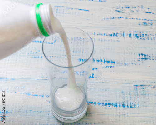 Pouring kefir, sour-milk product into a glass on a wooden background.