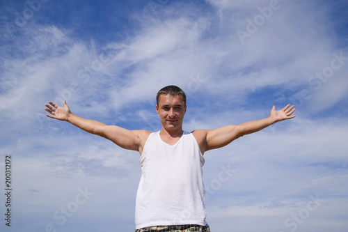 man in a white T-shirt laid his hands wide against the blue sky with clouds.