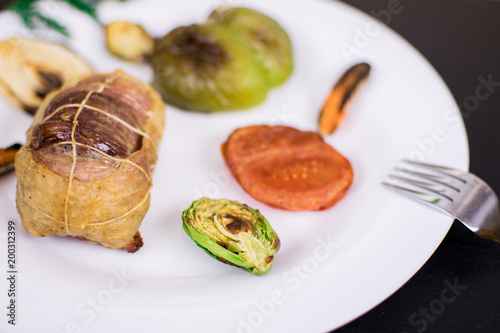 Cutlet from meat with grilled vegetables on a white plate and against a dark background.