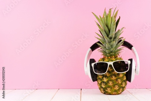 Hipster pineapple with sunglasses and headphones against a pink background. Minimal summer concept.
