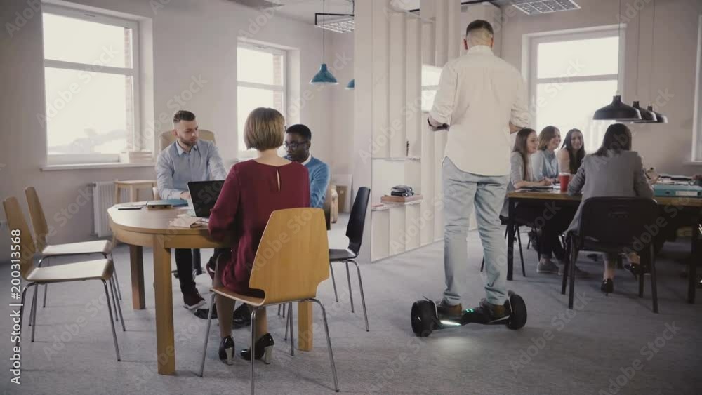 Young male boss using hoverboard to come and talk to colleagues. Confident leader uses technology in modern office 4K. Young male boss using hoverboard to come and talk to colleagues. Confident leader uses technology in modern office 4K.