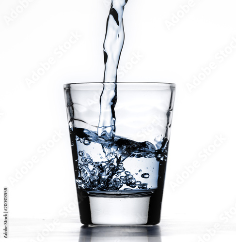 Small glass alcohol shot cup,  being filled with blue water, or liquid, closeup, white background with reflection