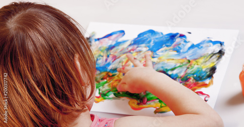 Little cute child girl holding a paint brush and painting on a white wall background (Creativity, education, child development in art, happy childhood, abilities concept)