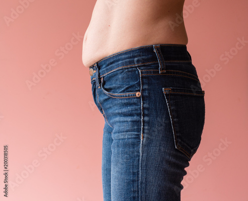 Side view of natural looking middle aged woman's stomach and hips against peach pink background