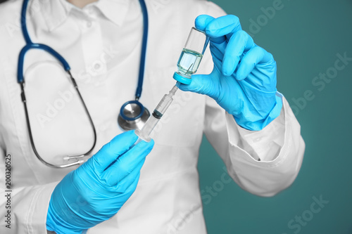 Doctor with syringe and medicine for vaccination on color background