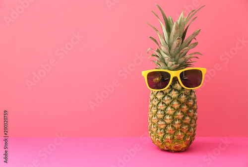 Fresh ripe pineapple with sunglasses on color background