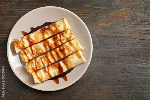 Thin pancakes served with chocolate syrup on plate, top view