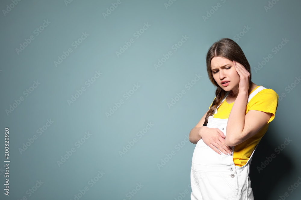 Young pregnant woman suffering from headache on color background Young pregnant woman suffering from headache on color background
