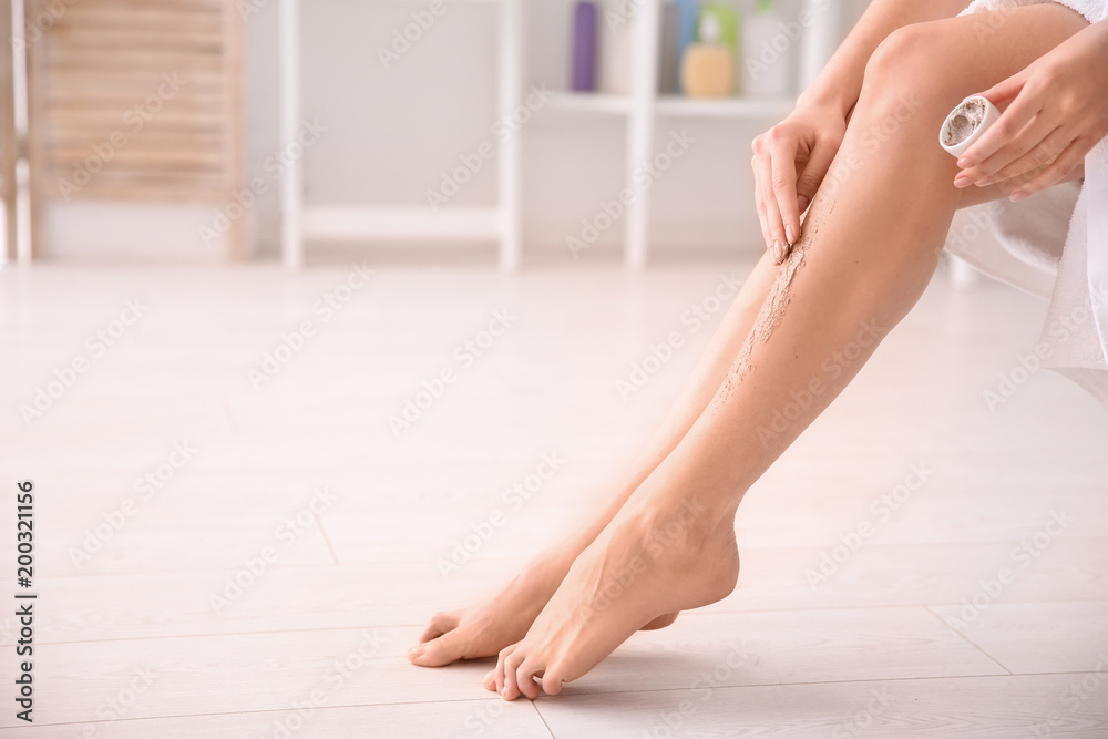 Fototapeta premium Woman applying body scrub on legs at home