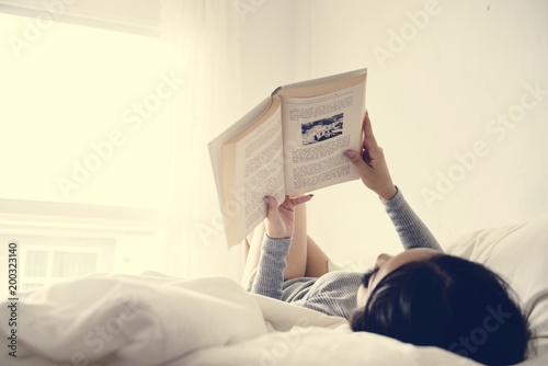 An Asian Woman Reading on a Bed in a Bright Minimal Room
