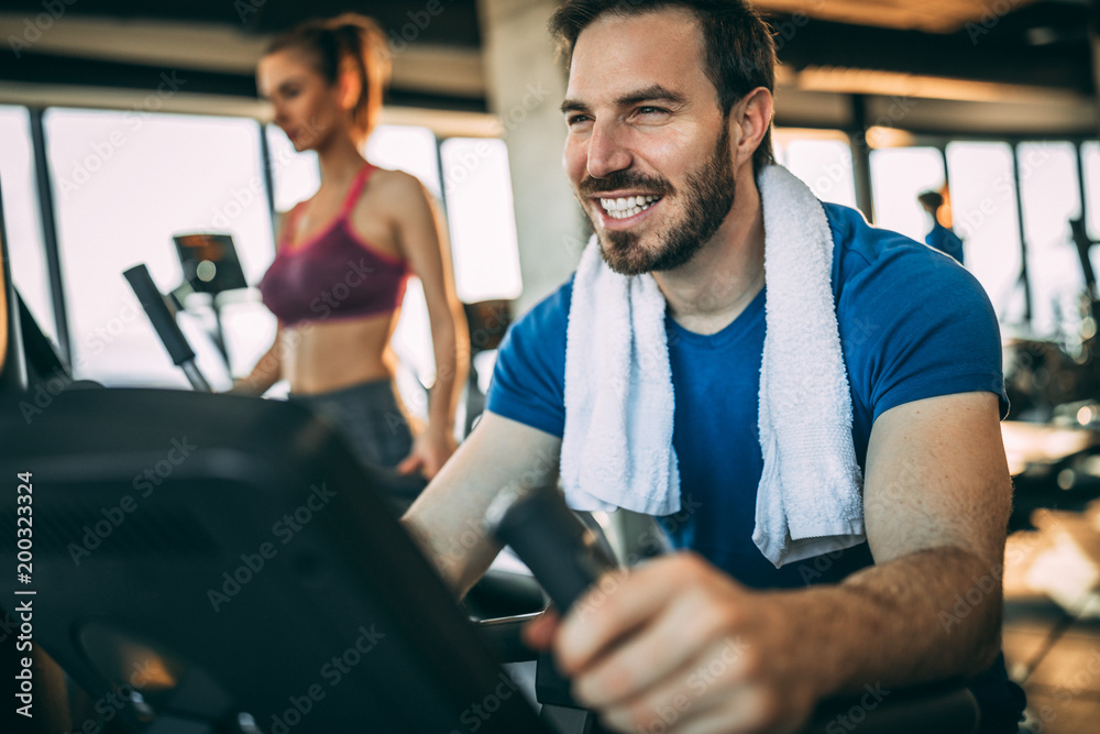 Obraz premium Happy mid adult man having fun in the gym. Bicycle for better cardio workout.