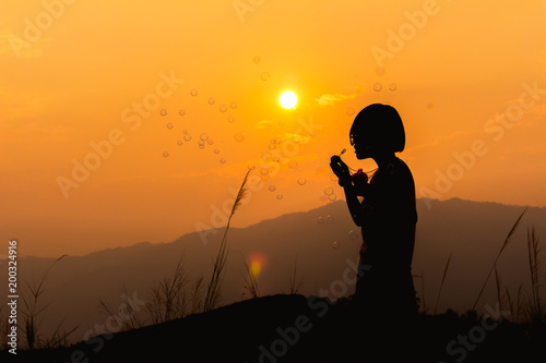 Silhouette little girl playing with bubble wand on mountain at sunset background