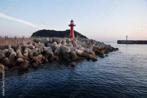 Red and white lighthouse at a seawall with wavebreakers in the deep bleue sea in Seogwipo, Jeju Island, South Korea photo