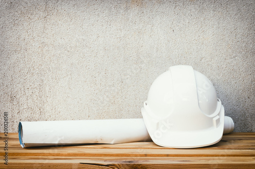 white safety helmet plastic and paper roll plan blueprint construction of engineering on wood floor table background with copy space add text