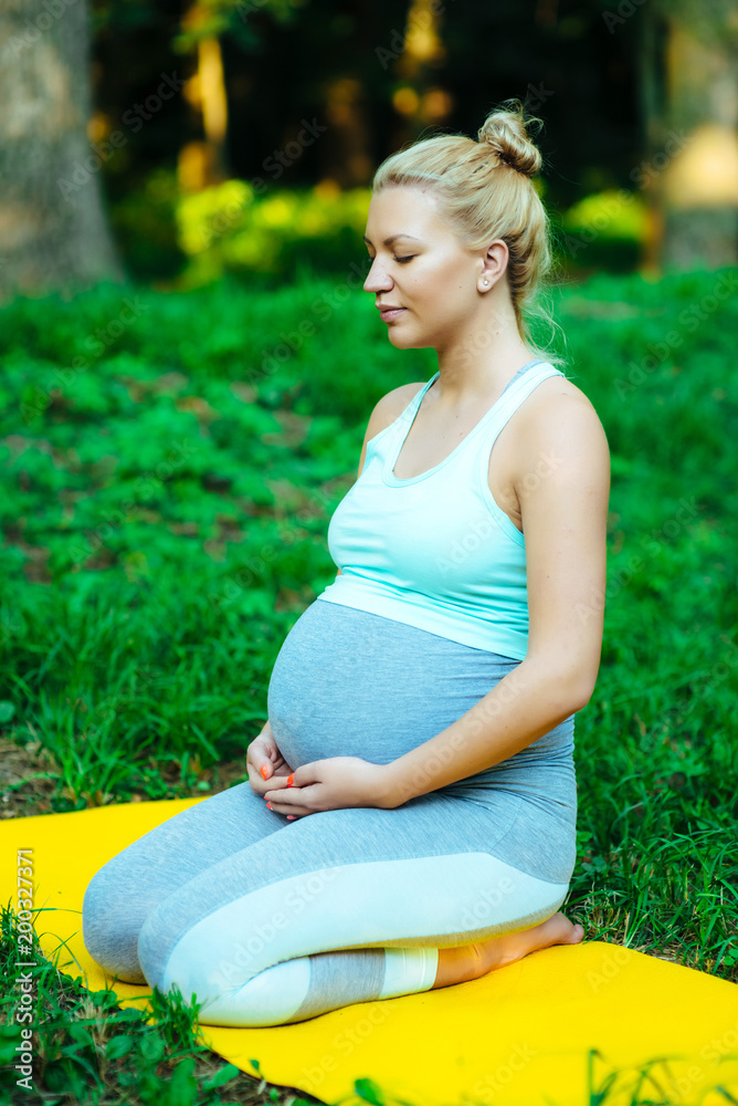 Pregnant girl sitting on a yoga mat in the park after training