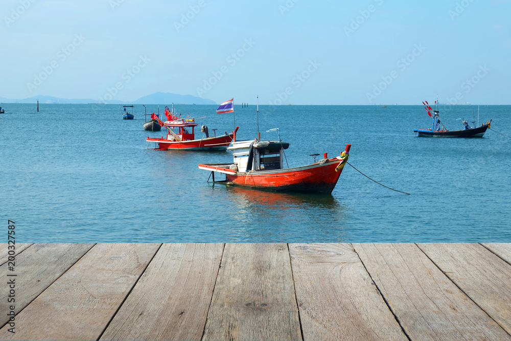 Wooden foreground with Fishing boats lie at anchor by the sea, with Blue sky and clouds background, copy space