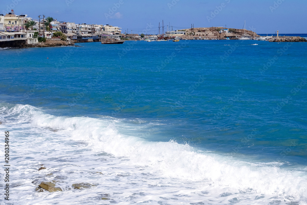 blue sea on a sunny day; White waves are at the forefront, but ships, boats and yachts are visible in the distance.
