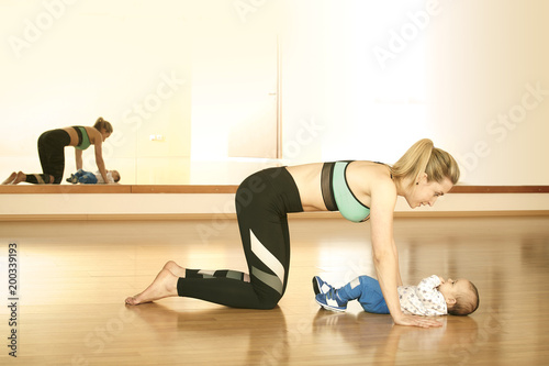 Mirroring young fitness woman exercising with her infant son