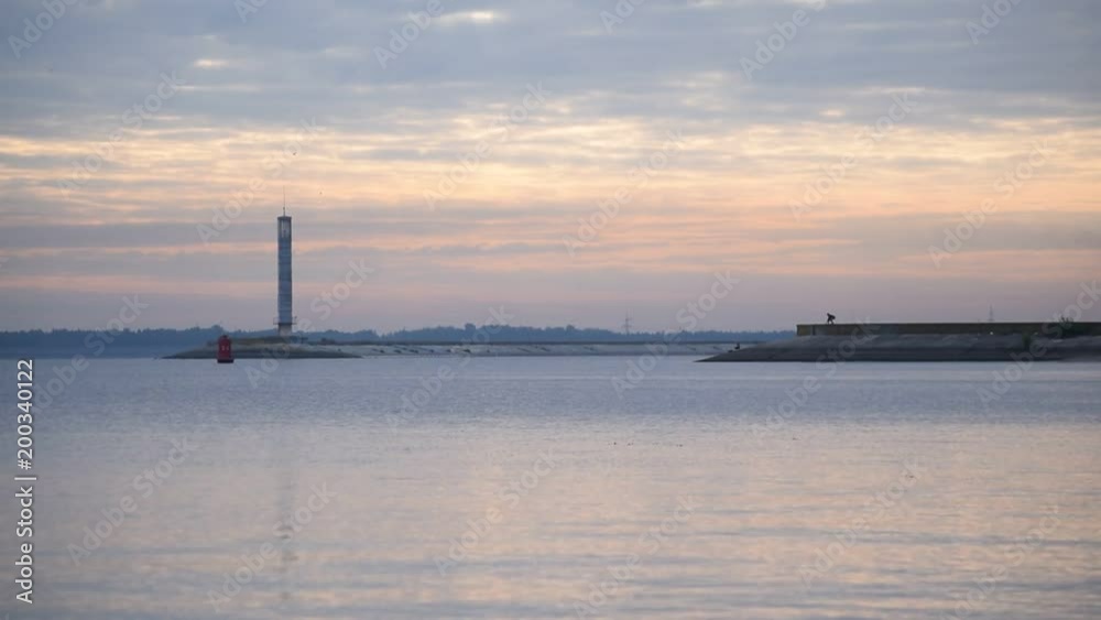 Beautiful cloudscape at dawn with colorful cirrus and cumulus clouds and lighthouse on breakwater and water surface with reflections of light. Shot on Dnieper river Beautiful cloudscape at dawn with colorful cirrus and cumulus clouds and lighthouse on breakwater and water surface with reflections of light. Shot on Dnieper river