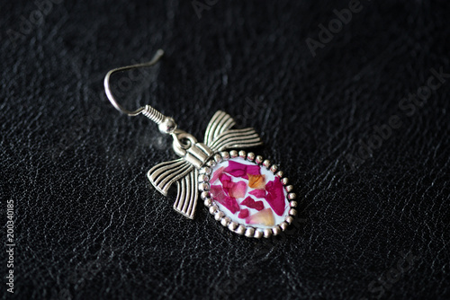 Epoxy resin earrings with dry rose petals on a dark background close up