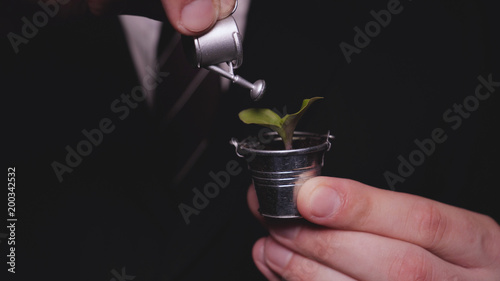 A businessman in a suit holds a sprout in a mini bucket and a watering can, a black background, a career growth, a new life.