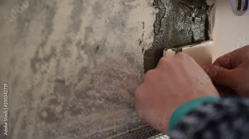 Hands of a tile worker gluing square tiles to a wall indoors