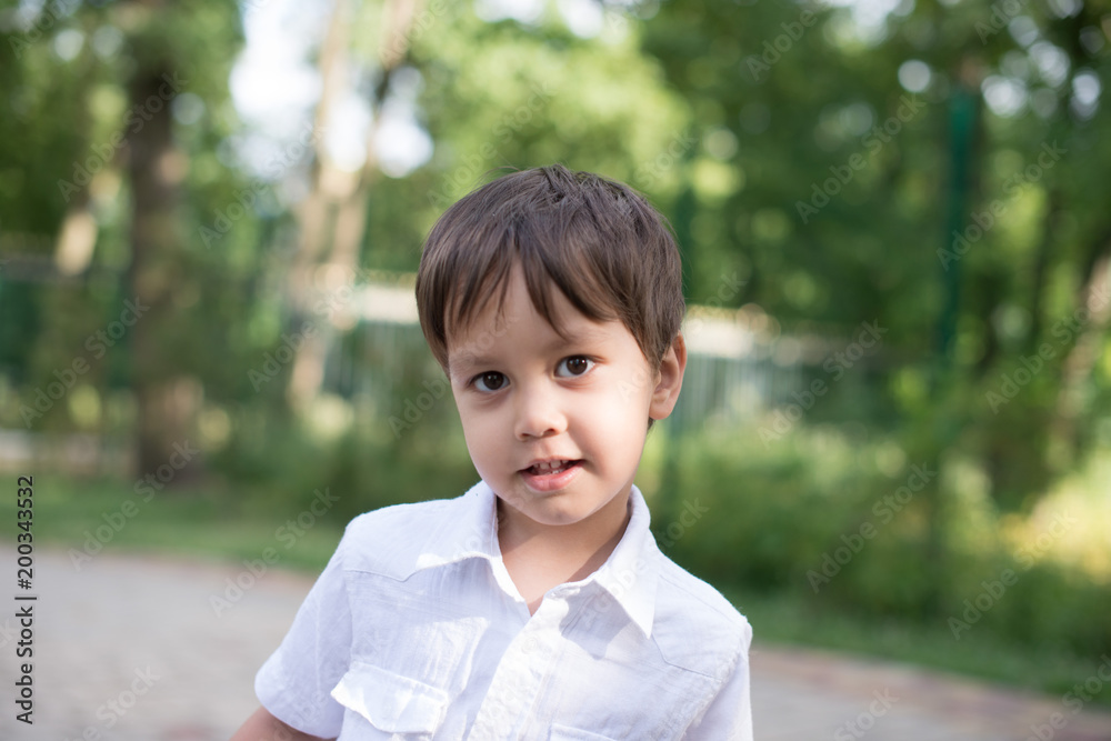 Close up emotional portrait of the smiling of the little blonde boy wearing white shirt in a park. Close up emotional portrait of the smiling of the little blonde boy wearing white shirt in a park.
