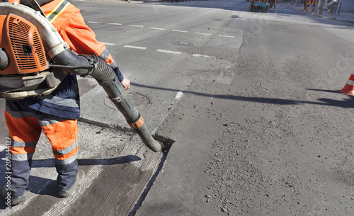 Partial repair of the asphalt road. The worker cleans the bad part of the road with an industrial vacuum cleaner