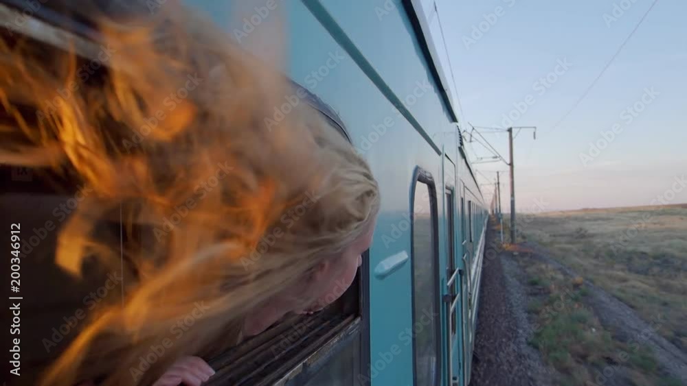 Woman riding train with blond hair blowing in the wind at sunset