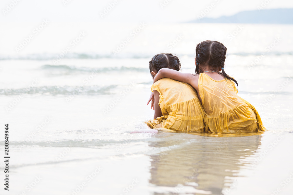 Back view of two cute asian little child girls hugging and having fun to play on beach together in summer vacation