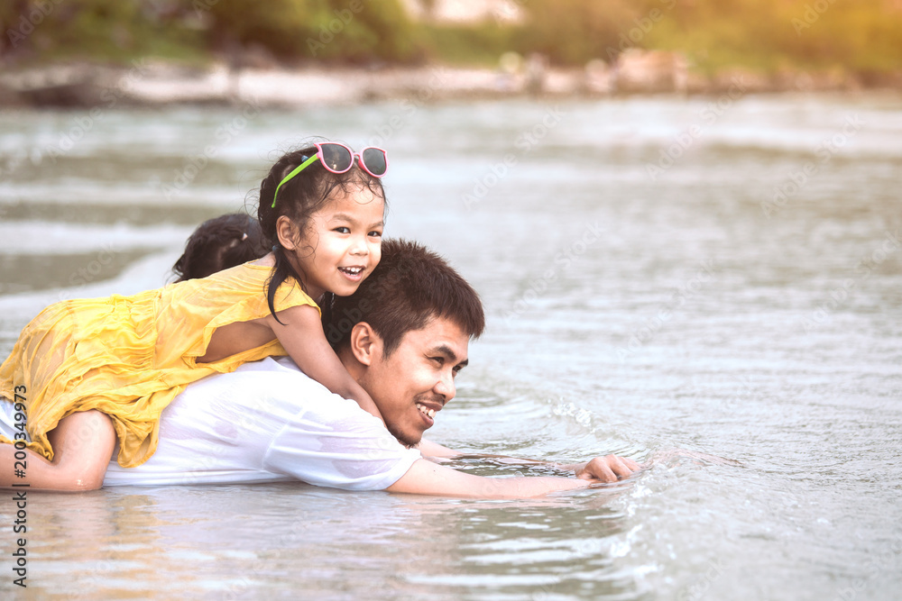 Fototapeta premium Cute asian little child girl hugging and riding on father and playing together on the beach with fun and love in summer vacation