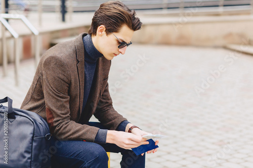 stylish attractive guy in jacket with passport and tickets