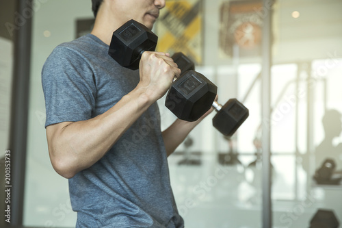 Fotografie Young man beginner exercising with dumbbell flexing muscles at gym, sport traini