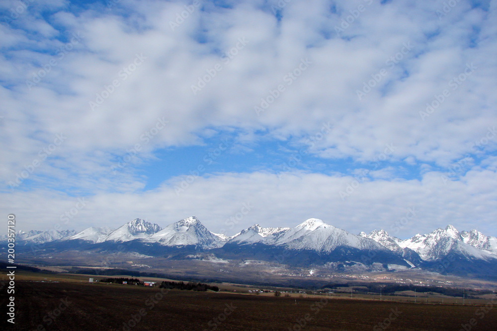 the landscape of the cloudy blue sky above the snow-capped peaks of the mountain range of the High Tatras in Slovakia.