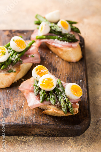 Fresh sendwich with ham, asparagus and quail eggs on old wooden chopping board. Easter spring breakfast concept with copy space.