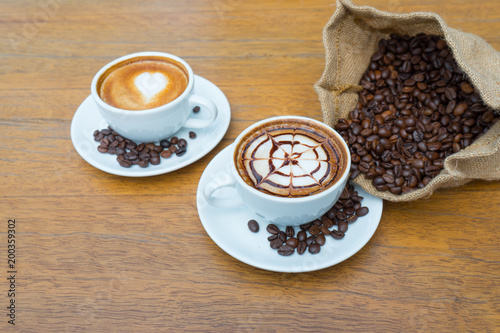 Top view, Two cup of latte coffee art with coffee beans in sack on wooden table