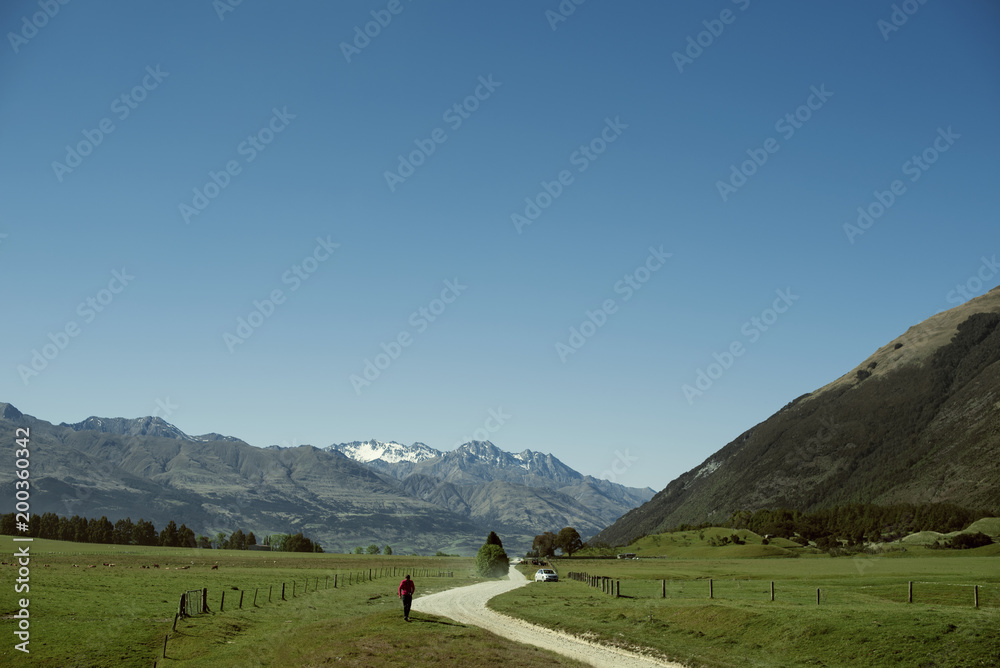 Senderista con mochila andando por un camino junto a una montaña hacia un coche	