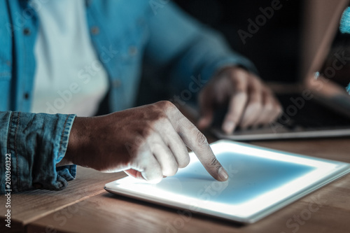 Sophisticated technology. Young smooth male hands placing finger on sensor screen of tablet which lies on wooden surface